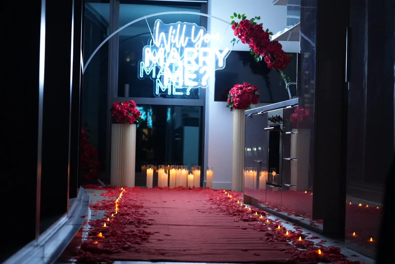 Candlelit red carpet aisle and neon Will You Marry Me sign inside a dark Melbourne apartment at night